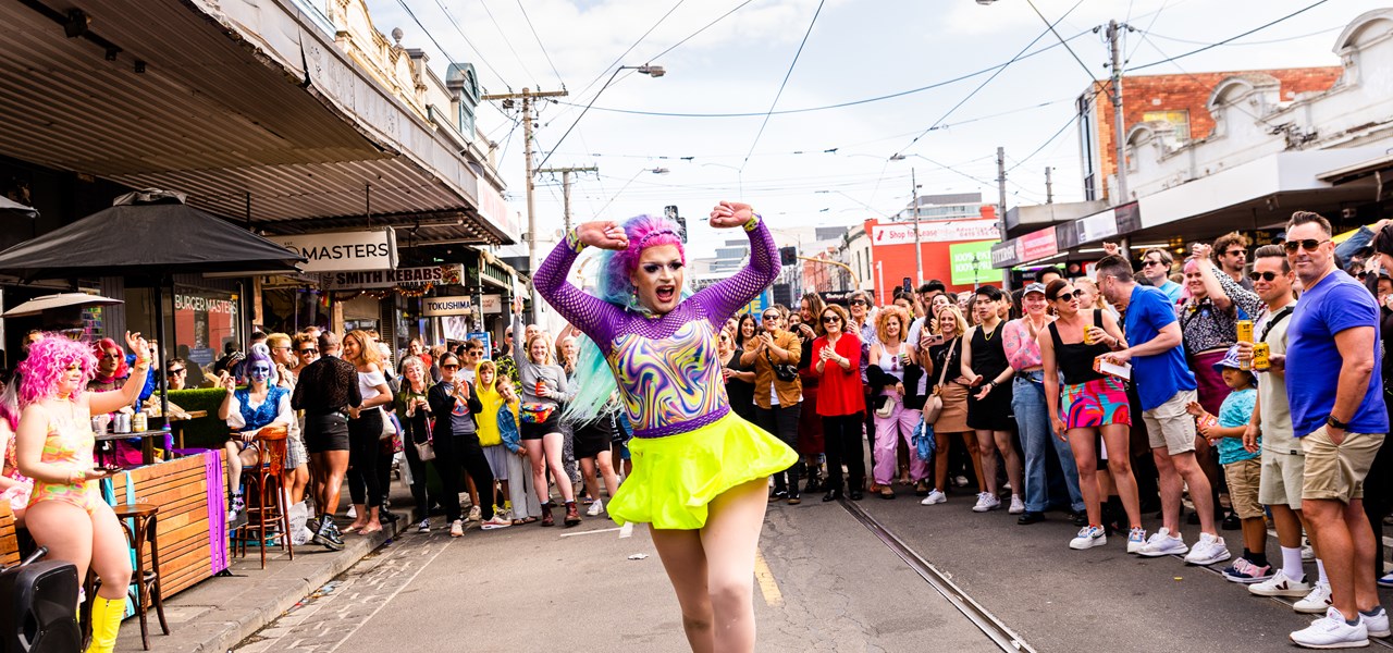 Person in drag wearing a short yellow dress and performing in the middle of the street.