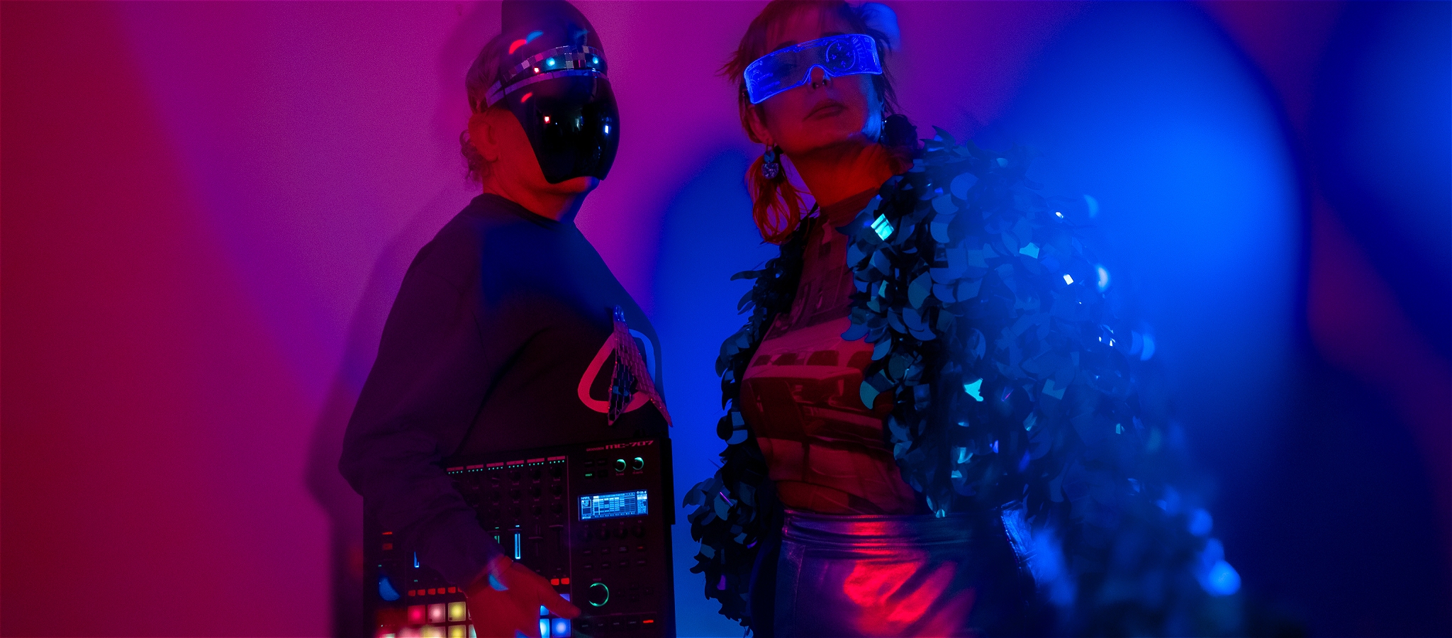person in robot mask holding synthesizer person in cyber glasses standing