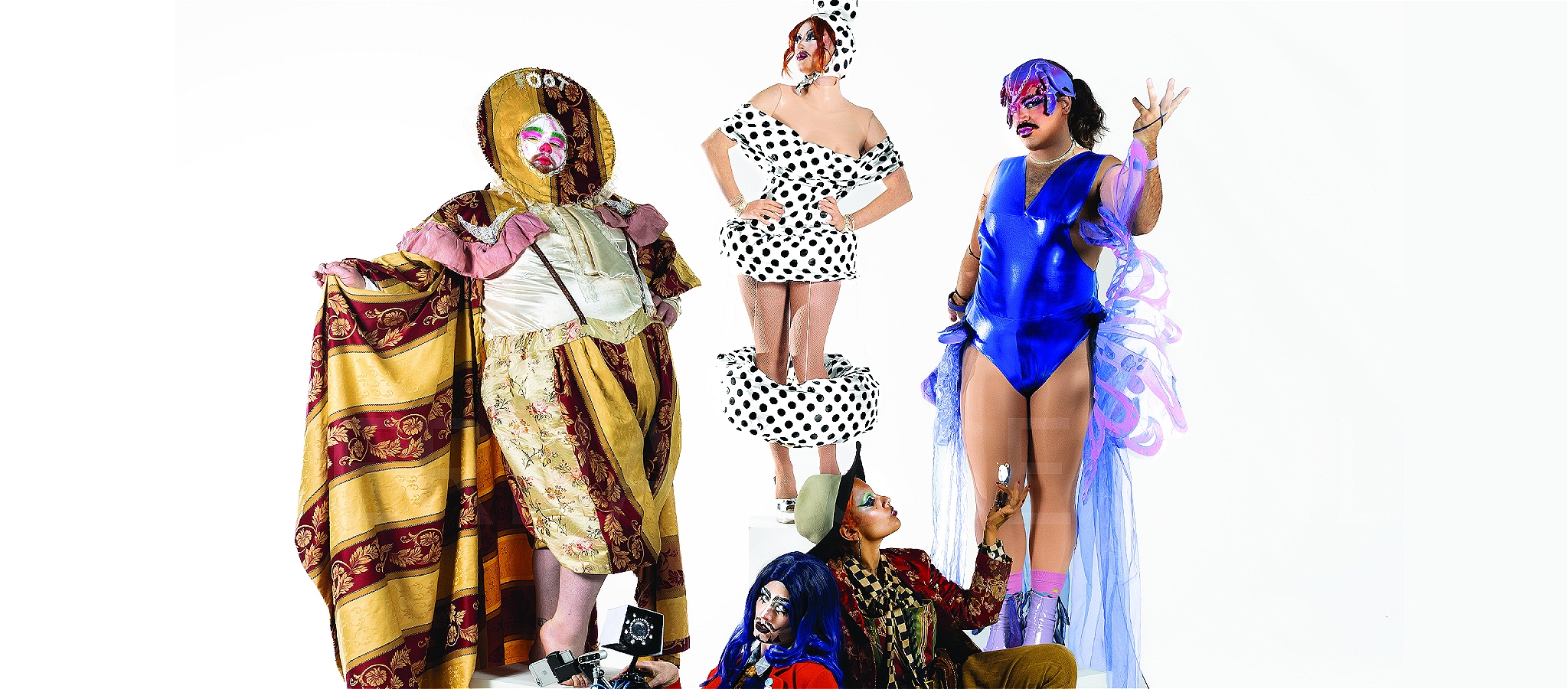 Five performers in eccentric patterned costumes standing on plinths against a white background.