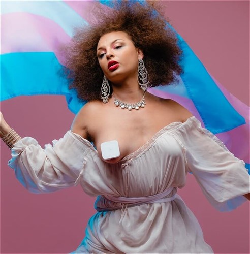 Person elegantly dressed in white, with one boob hanging out (but covered), waving a Trans flag