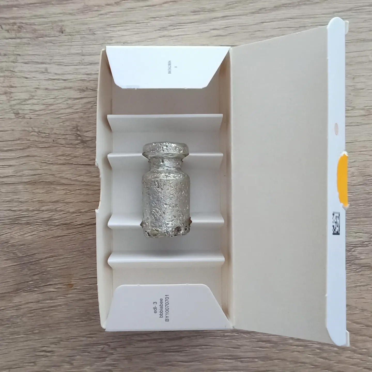 Sculpture of a small metallic silver object fitted into a cardboard box