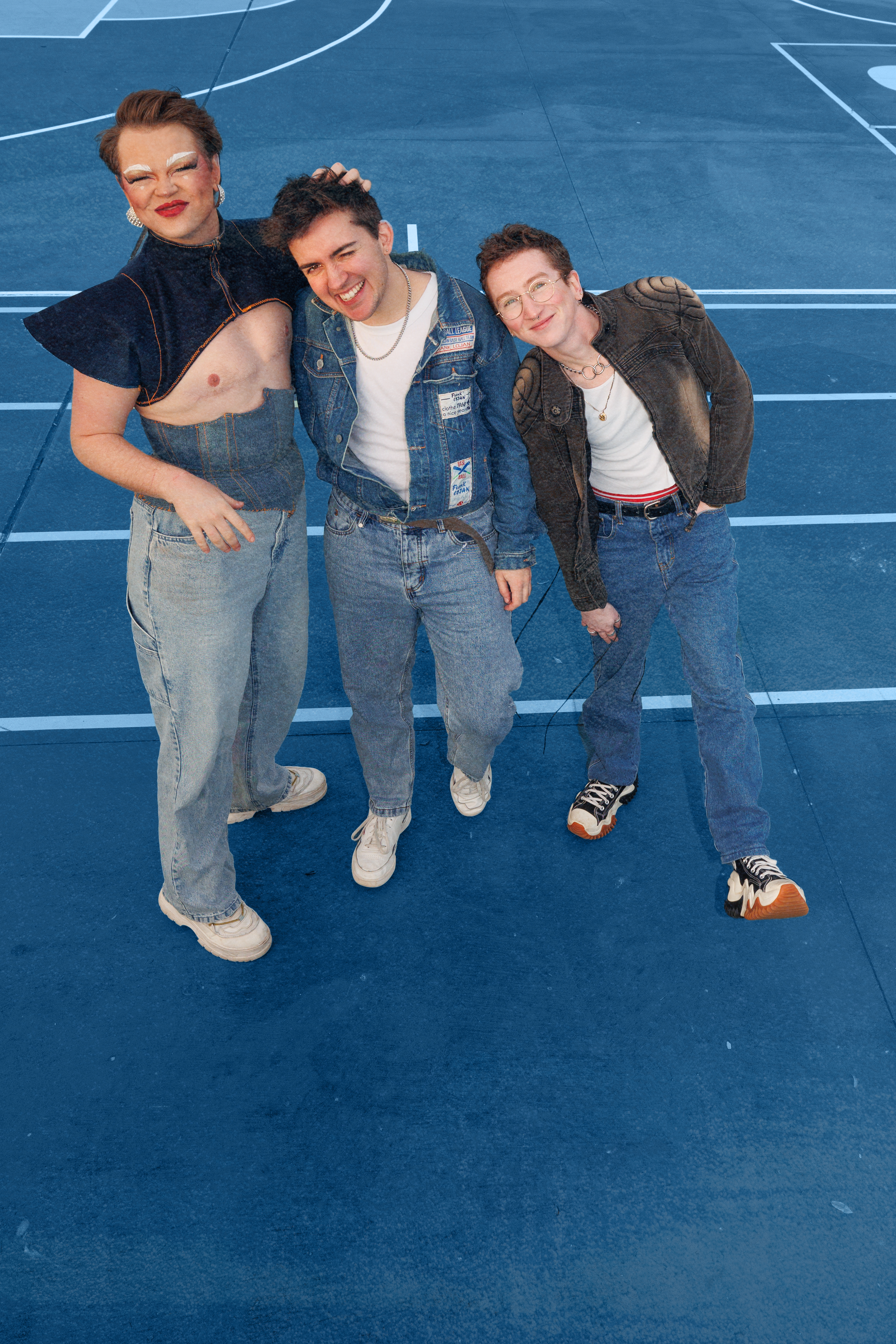 HRTthrob the band's three members dressed in denim smileup at the camera on a blue sports court with white lines.