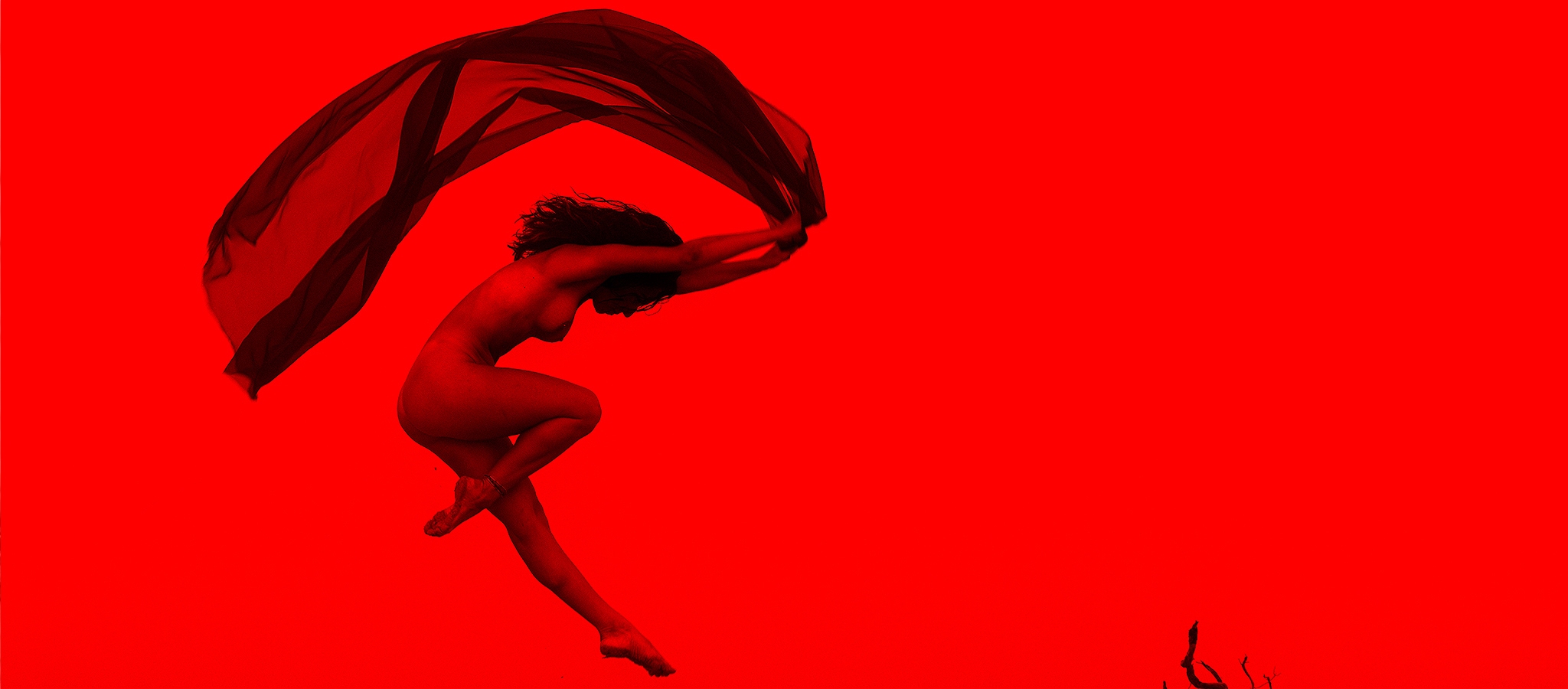 A red and black rendered photograph of a feminine figure leaping nude through the air holding a shear dark fabric above her head