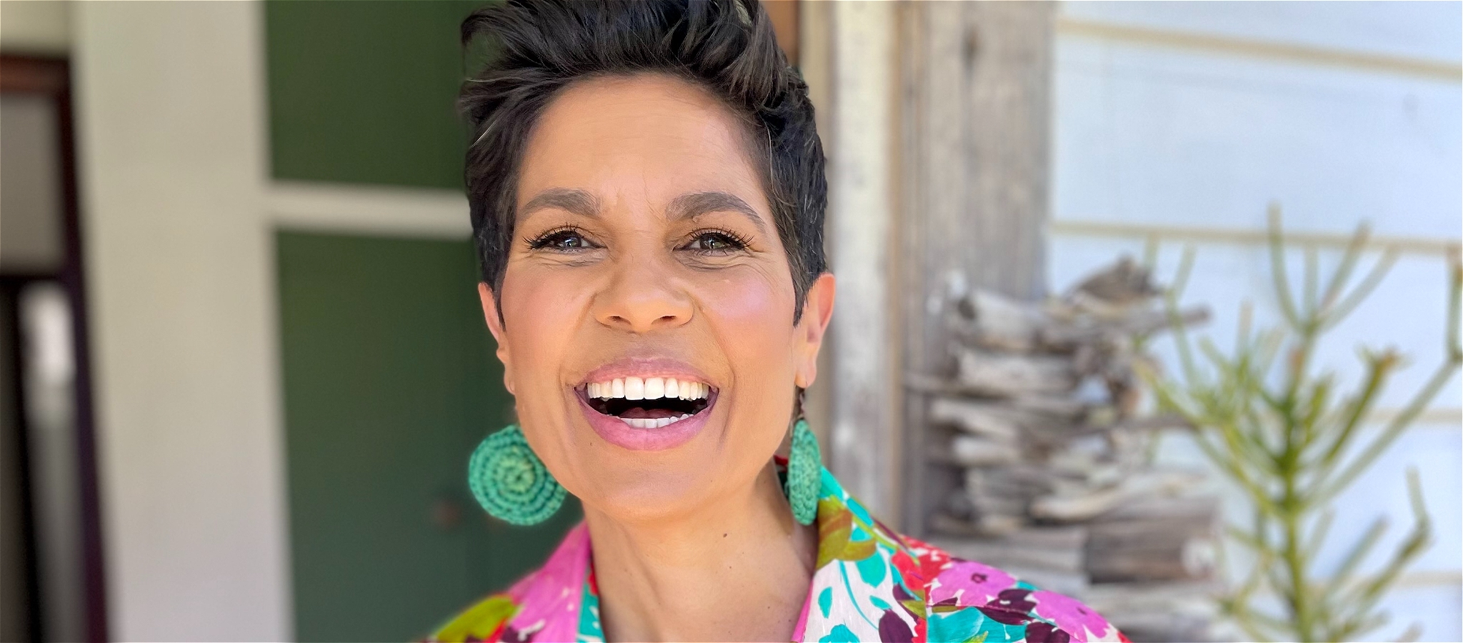 A person smiling broadly while standing outside the entrance of a house