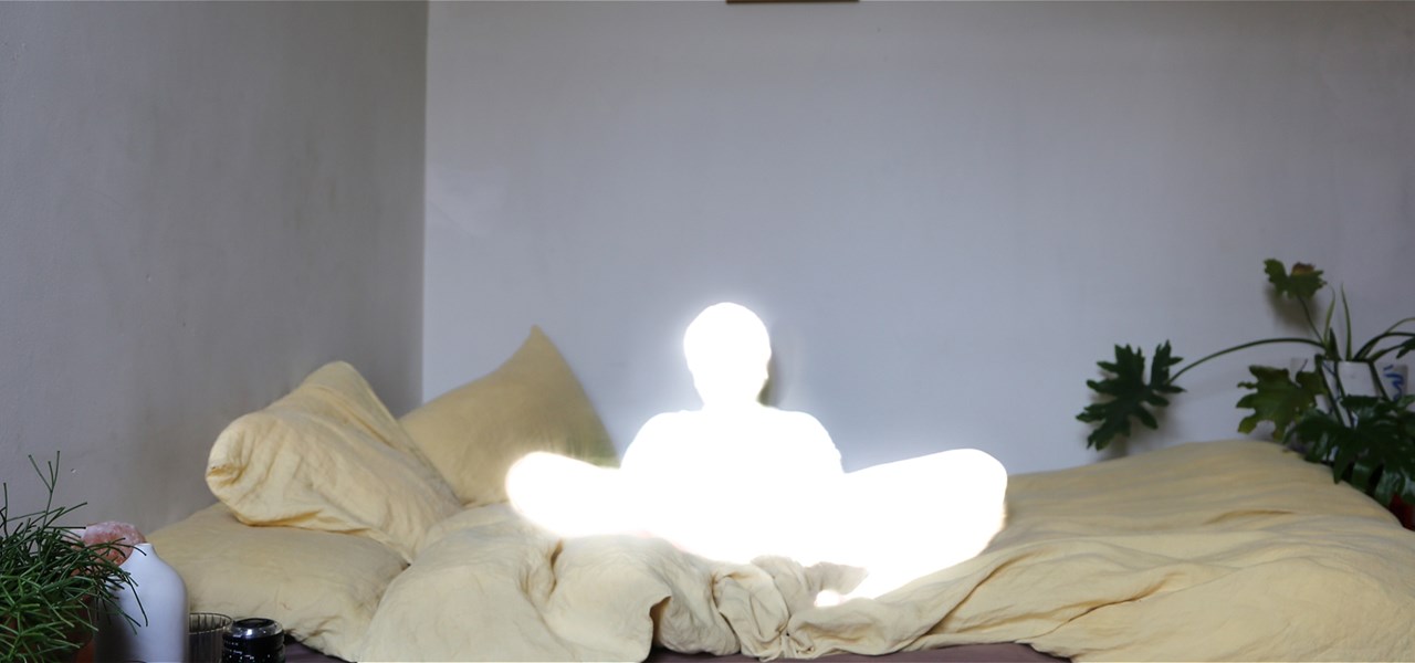 Illuminated person sitting crosslegged on a bed.