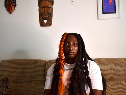 Headshot of Ayebatonye sitting on a couch with African indigenous art hanging in the background