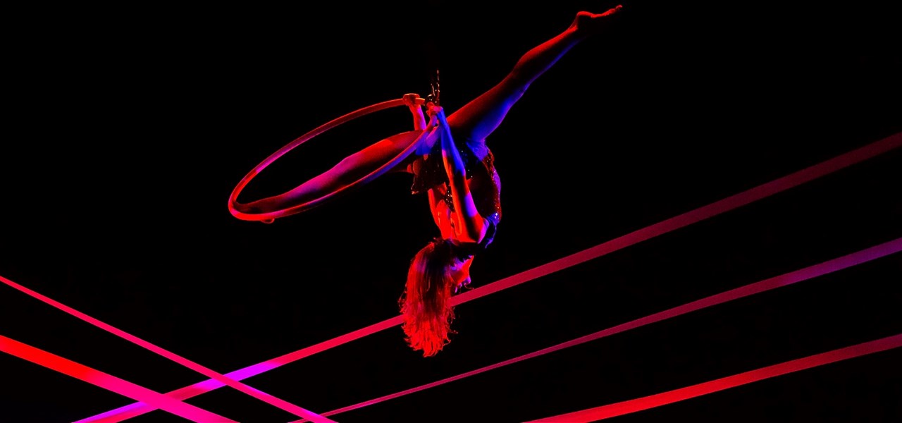 A woman performing the splits on aerial hoop with neon lights crossing in the background