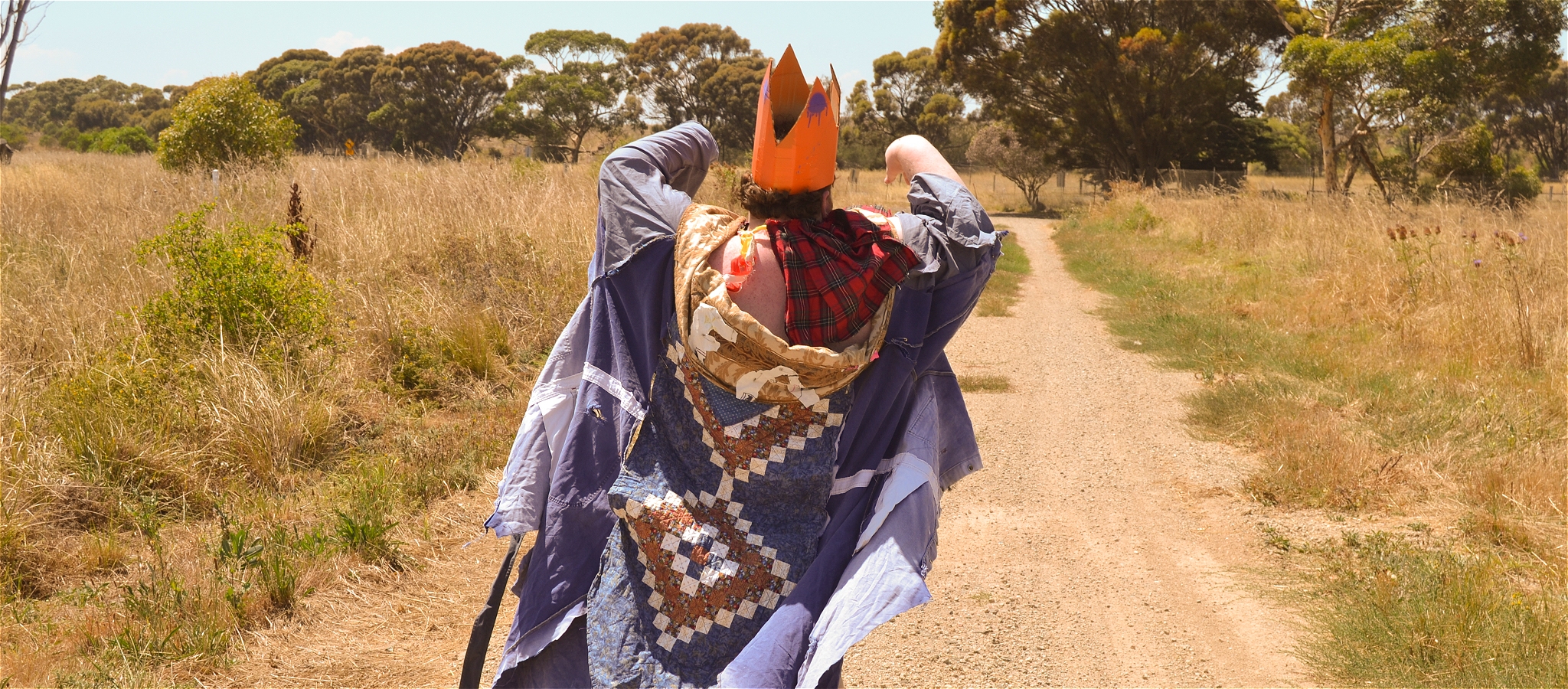 The Artist Known as Foot, curator of this exhibition, clothed in their textile wearables standing on a dirt road facing away from the camera