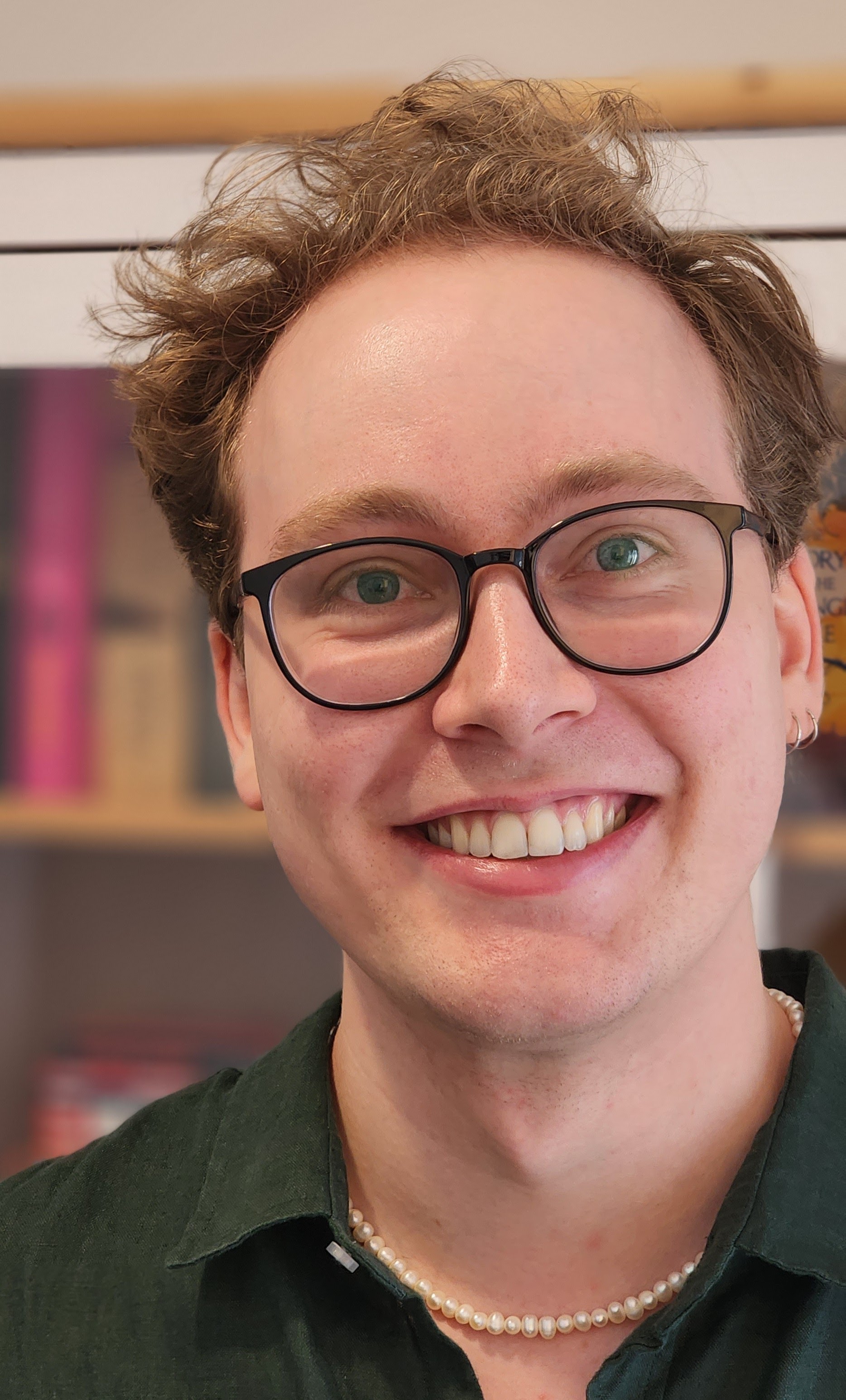 close up photo of a person smiling with short brown hair, black glasses and a pearl necklace