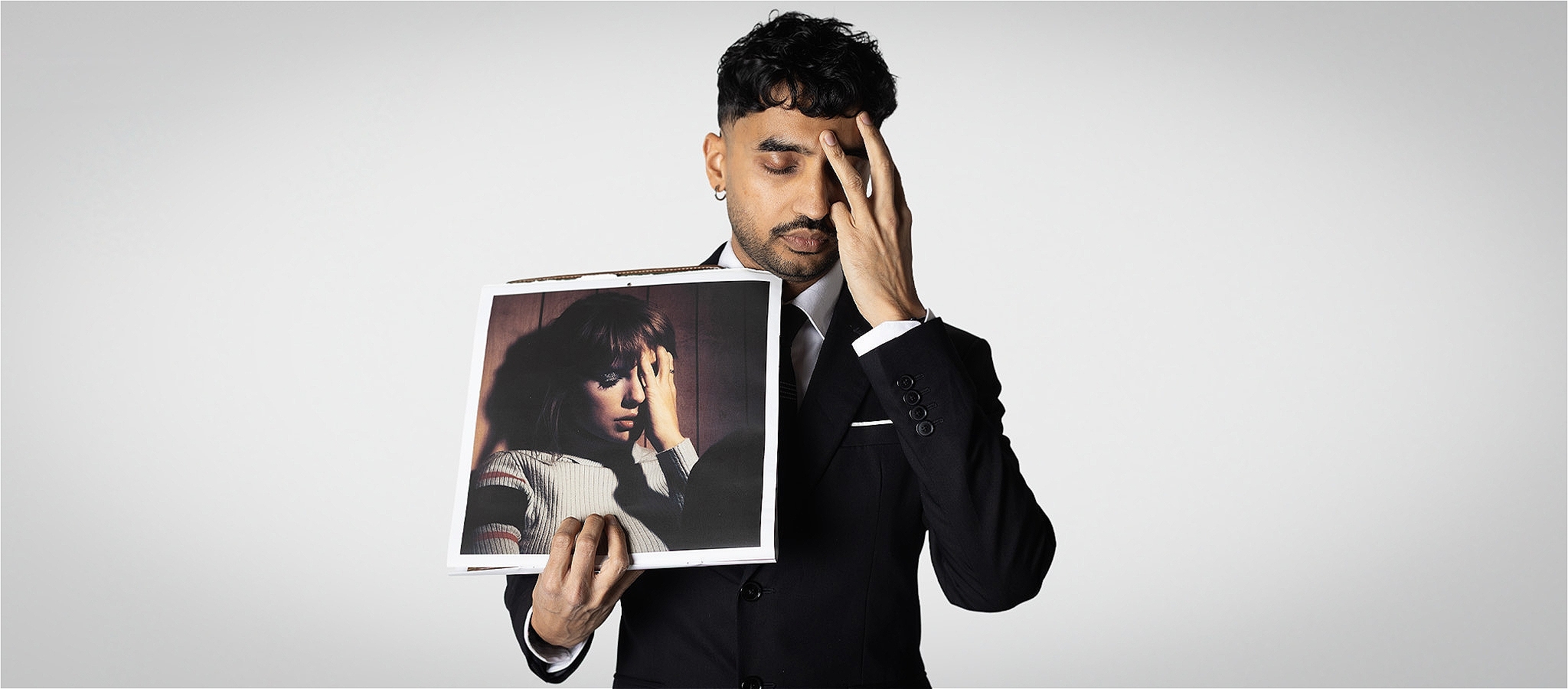 A photograph of the artist with their hand on their forehead, holding an image with of a person in the same pose.
