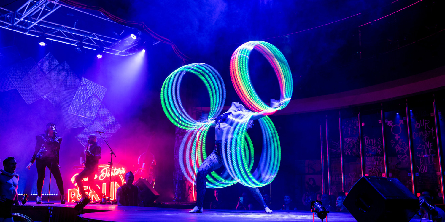 Circus performer twirling lots of hoops with an orchestra on the stage in the background