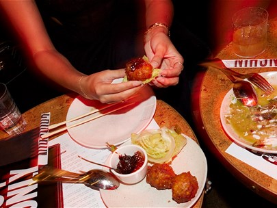 Restaurant table with several plates of food and one diner's arms reaching in