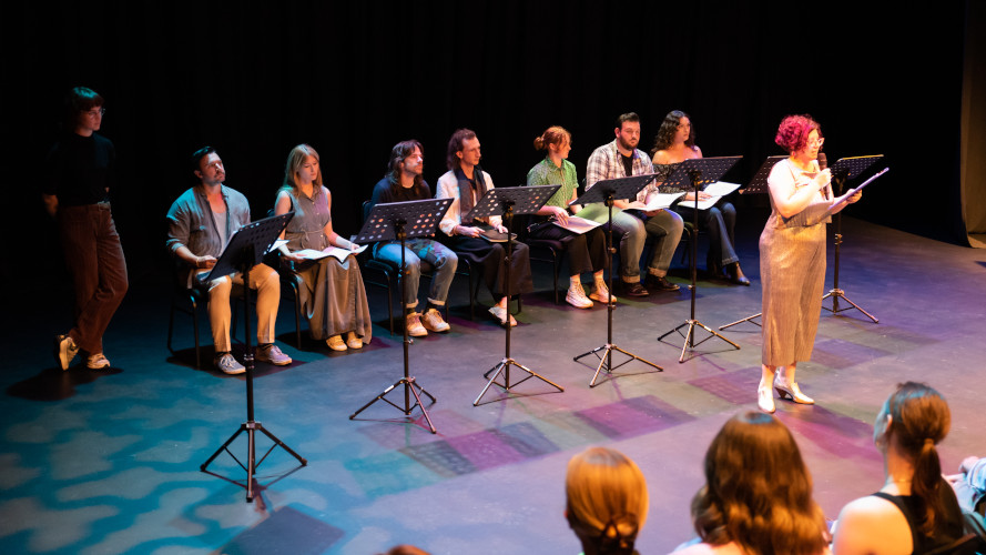 Creatives sitting on stage with the MC standing in front of them holding a microphone 