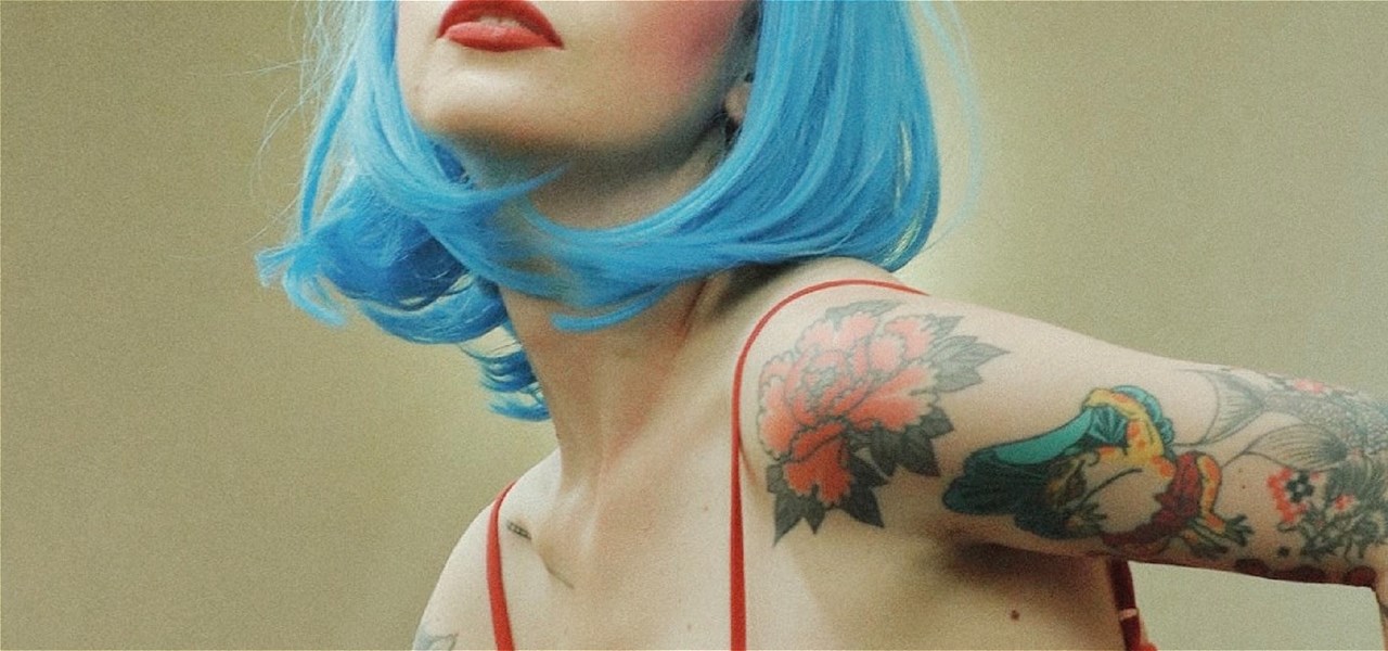 Image is of a person wearing a blue wig and a red bra with red lipstick and tatoos.