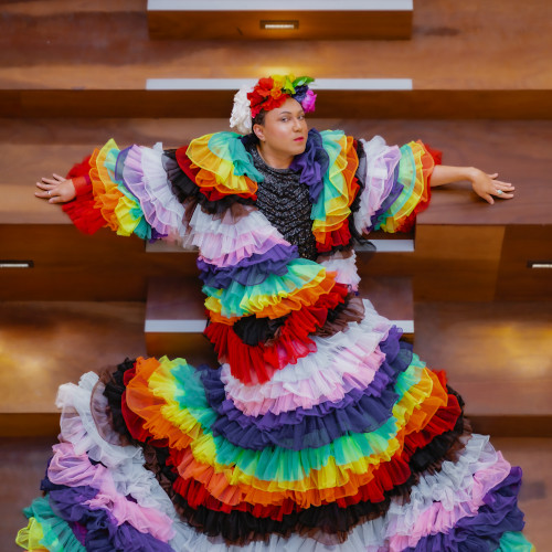 Mama Alto sitting on the Pride Centre stairs dressed in a frilly rainbow dress