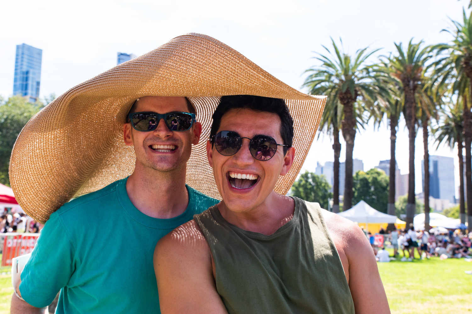 Two people hiding under a large hat and obviously having a ball at Midsumma Carnival