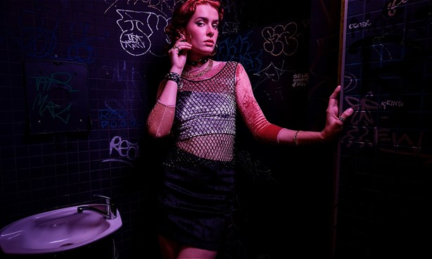 A person wearing a fish net top standing in a bathroom toilet in a night club.