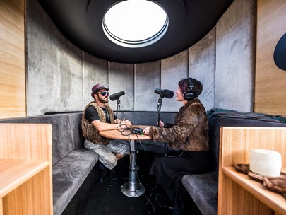 Two people sitting facing each other inside the Pridefinder mobile recording studio