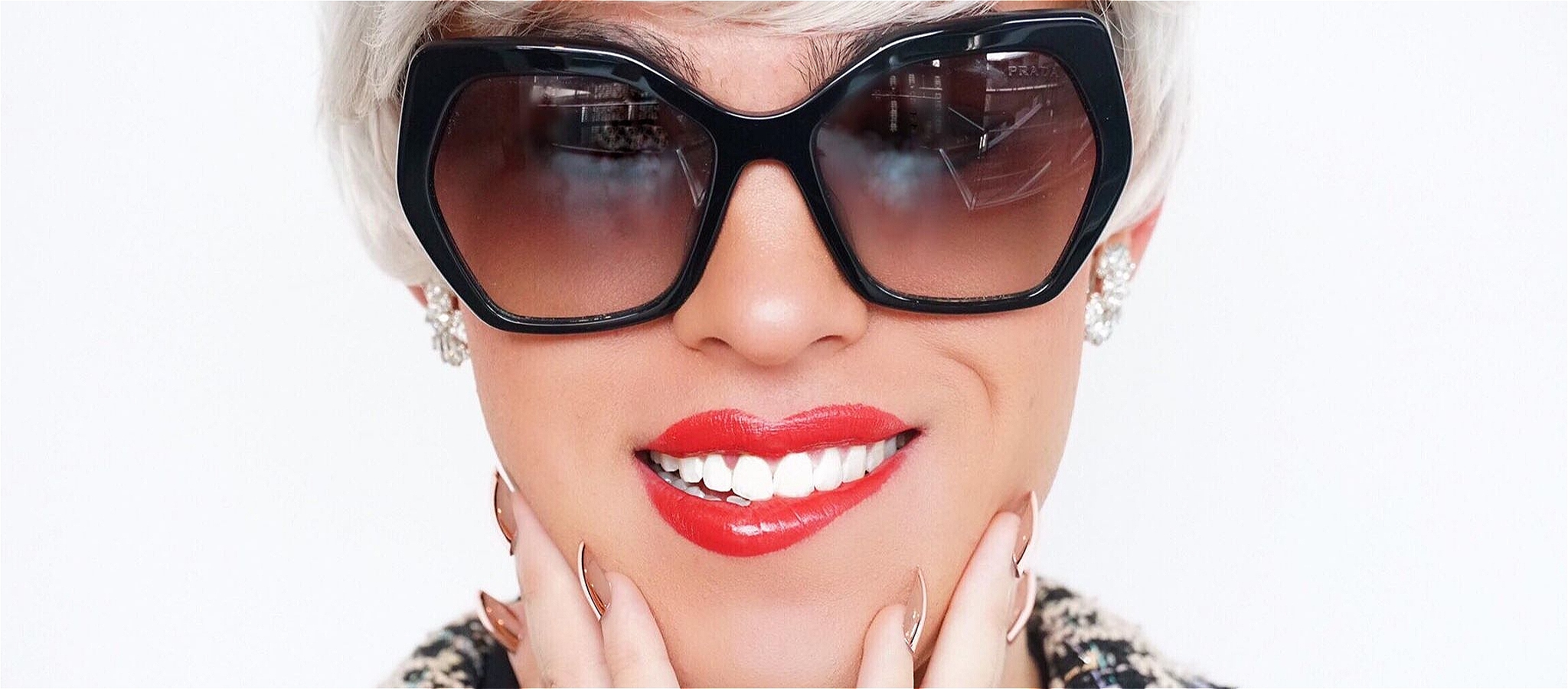 Headshot of a beautiful woman wearing fashionable jewellery and Prada sunglasses smiling at the camera