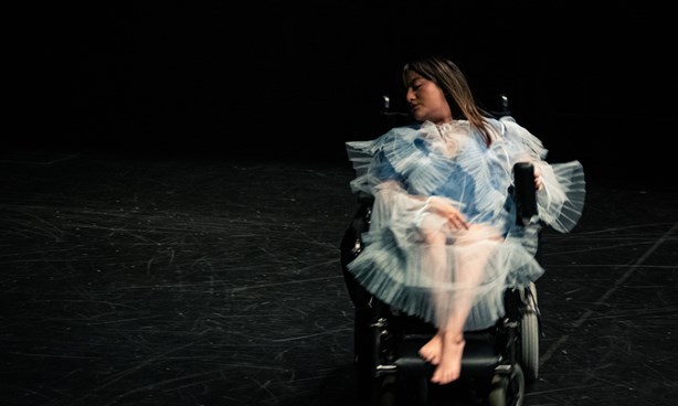A person in a wheelchair dressed in white lace in front of a black background