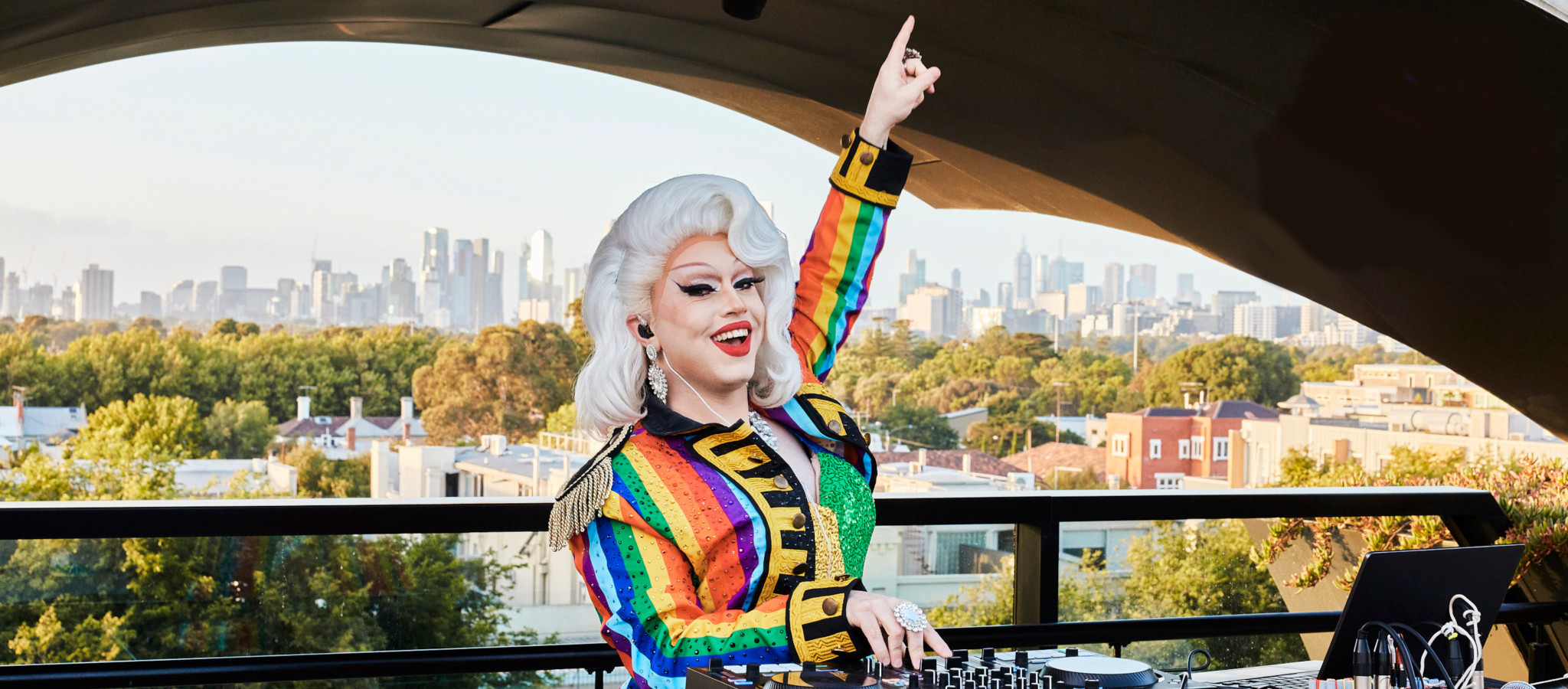 A DJ wearing a rainbow outfit and playing music on the Victorian Pride Centre rooftop