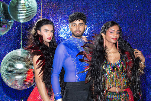 The Karma Dance trio standing in front of disco balls and a glittery blue background