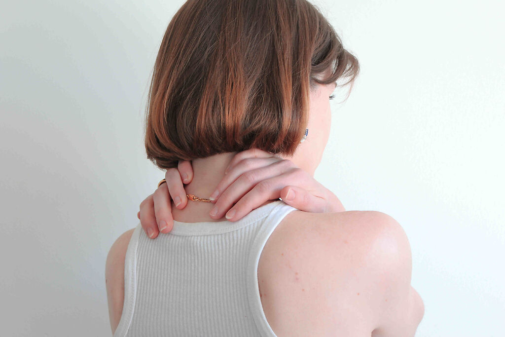 Person wearing a white singlet with their back to the camera clasping their hands around their neck