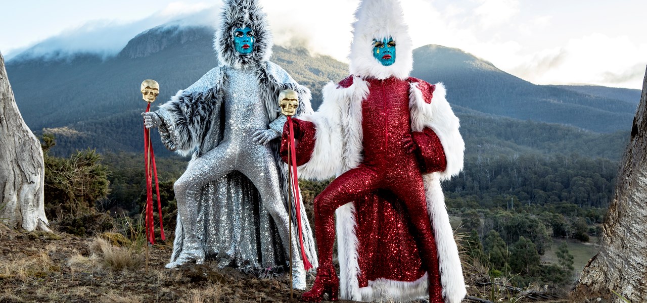 The Huxleys in a mountainous landscape, dressed in silver and red with faux-fur capes and headresses