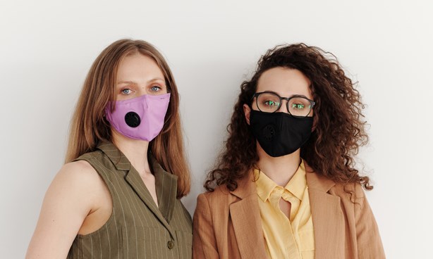 Two masked young, female-identifying people in brown outfits, one holding a folder