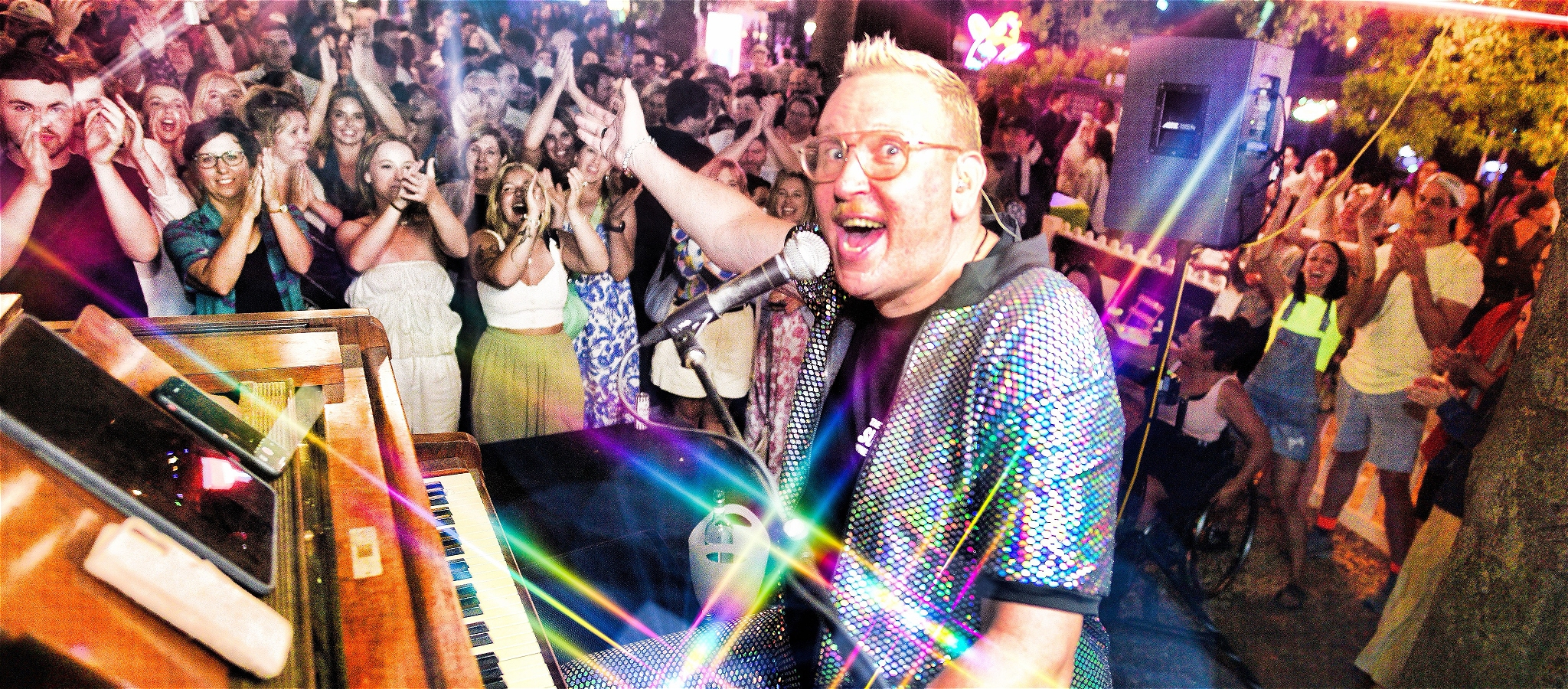 Trevor Jones sitting at the piano gesturing to the enthusiastic crowd behind him
