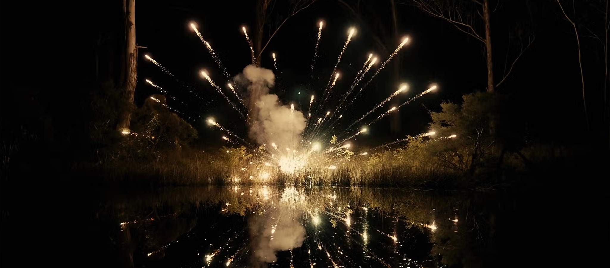 An explosion of fireworks rise into the night sky whilst being reflected below in nearby water