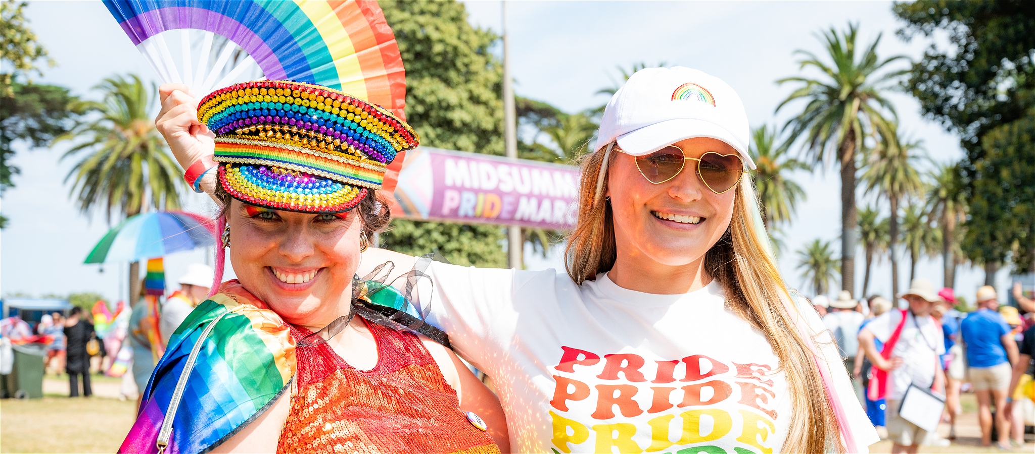 two people standing in front of the Pride March arch - dressed in pride colours
