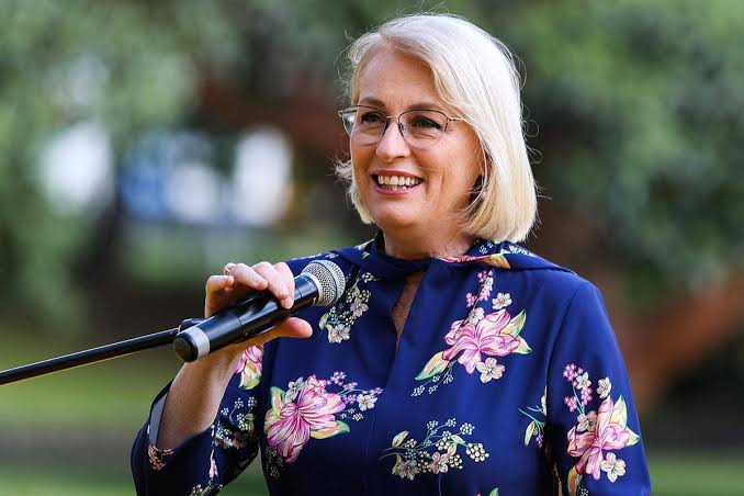 Photo of Sally Capp smiling as she speaks into a microphone - blurred outdoor setting behind her