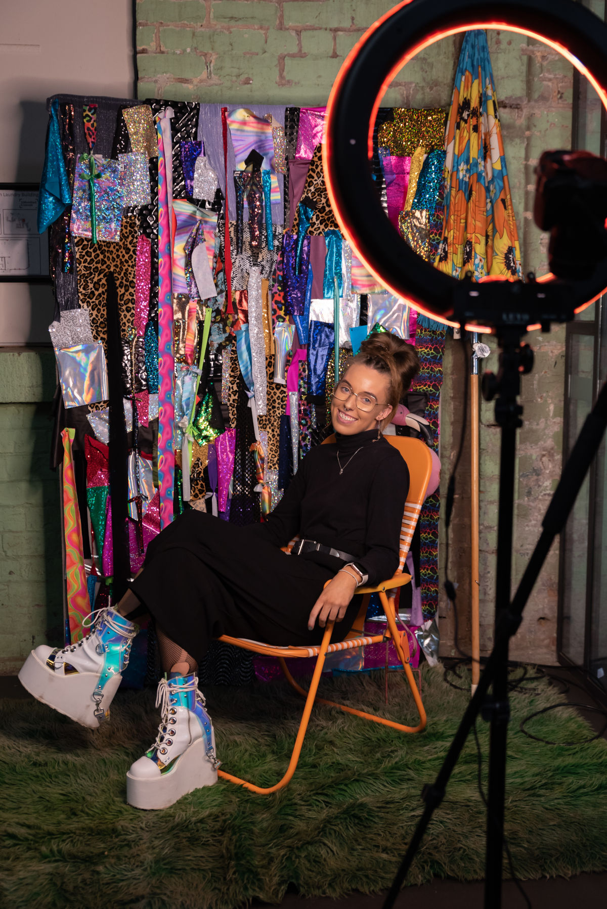 Woman dressed in black wearing white shoes will VERY large soles in front of a rack of colourful clothes