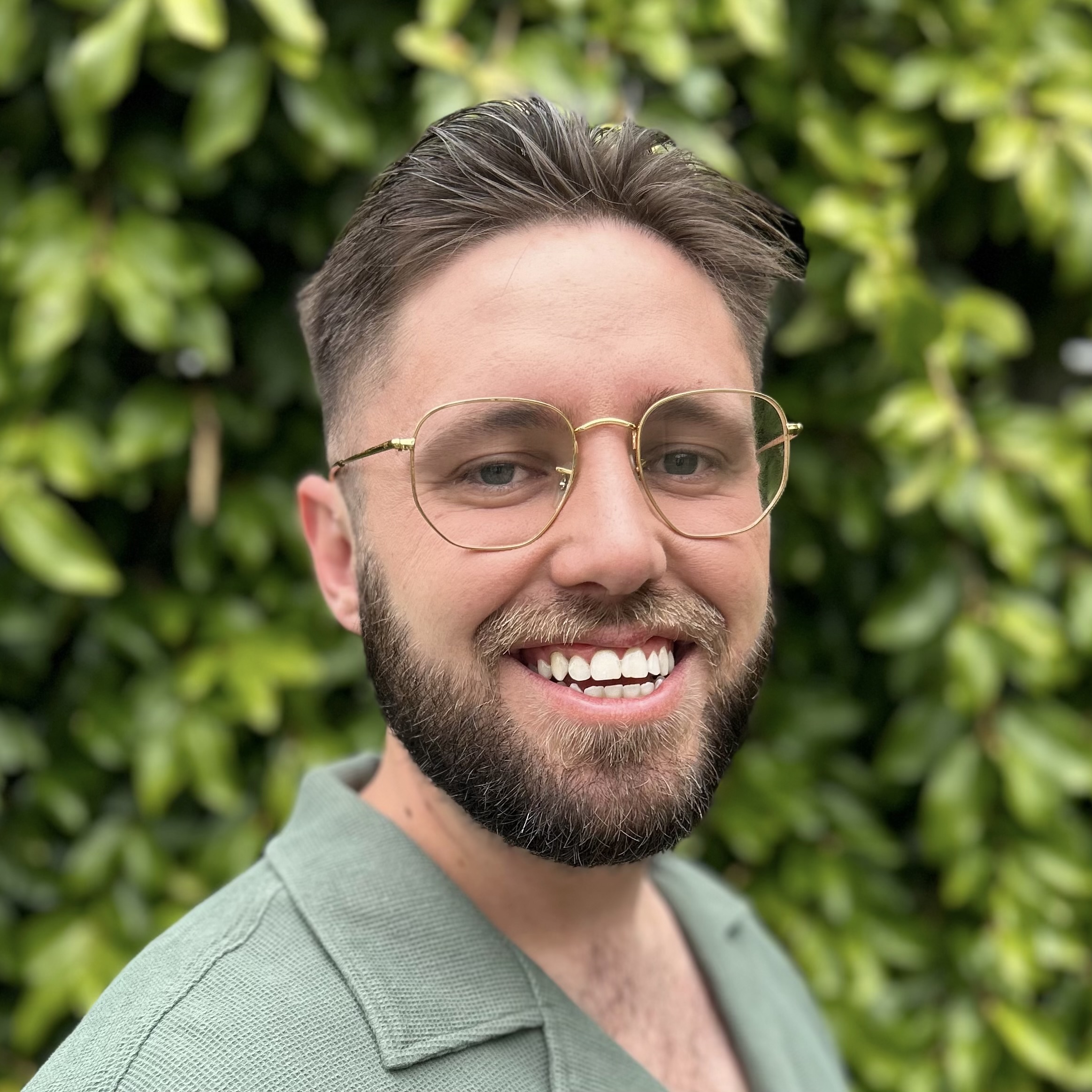 A person with light brown hair and beard wearing glasses and smiling.