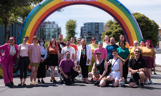 A crowd of people standing under a giant rainbow arch with text "Melbourne PRIDE"