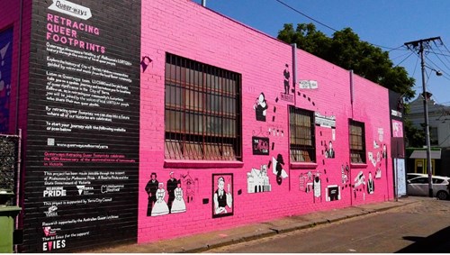 The finished product: RETRACING QUEER FOOTPRINTS text on left, graphics against a pink background on the outside of a building on the right