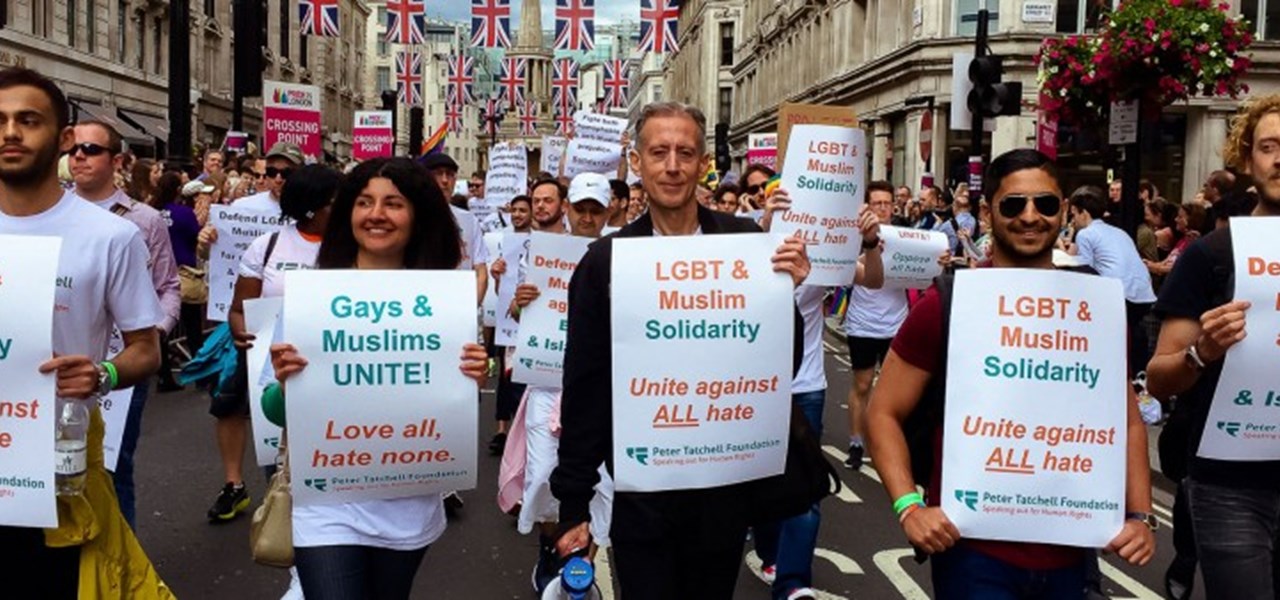 A street protest with lots of people holding signs about gays and muslims against hate