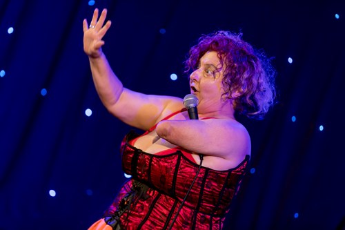 Kath Duncan on stage, holding a mic under one armpit and gesticulating to the audience