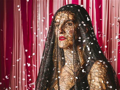 A woman with bright red lipstick wears a black veil as confetti showers down around her