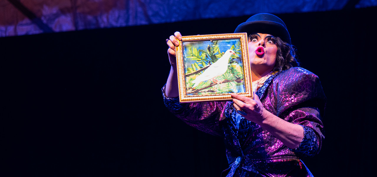Person dressed in a glamorous purple outfit with bright red pursed lips holding a photo of a white bird