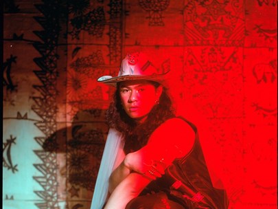 Julai squatting down, wearing a sombrero in front of an Indigenous-themed backdrop