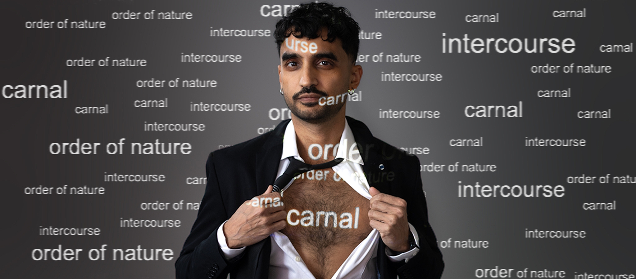 Performer wearing a suit with the shirt partly unbuttoned to expose the chest, with projections of the words CARNAL, INTERCOURSE, etc