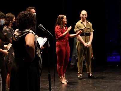 4 actors and 2 playwrights address an audience onstage in a black box theatre; the MC is in the foreground