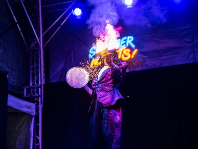 Circus performer on stage playing with fire with neon lights behind them.