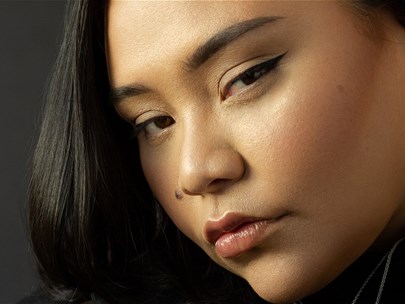 Headshot of an Asian person wearing silver earrings looking suspiciously towards the camera