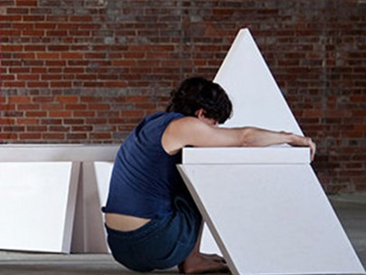 Gordon Hall squatting on the floor, surrounded by canvases