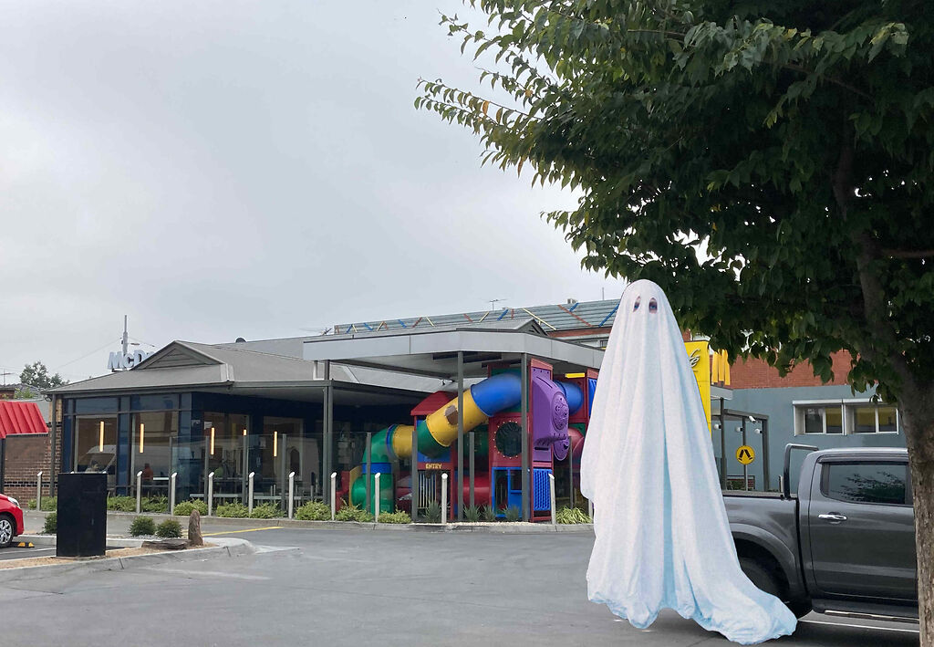 Ghost-like person in a sheet (with 2 eye holes) in the car park of a building (perhaps a retirement village)