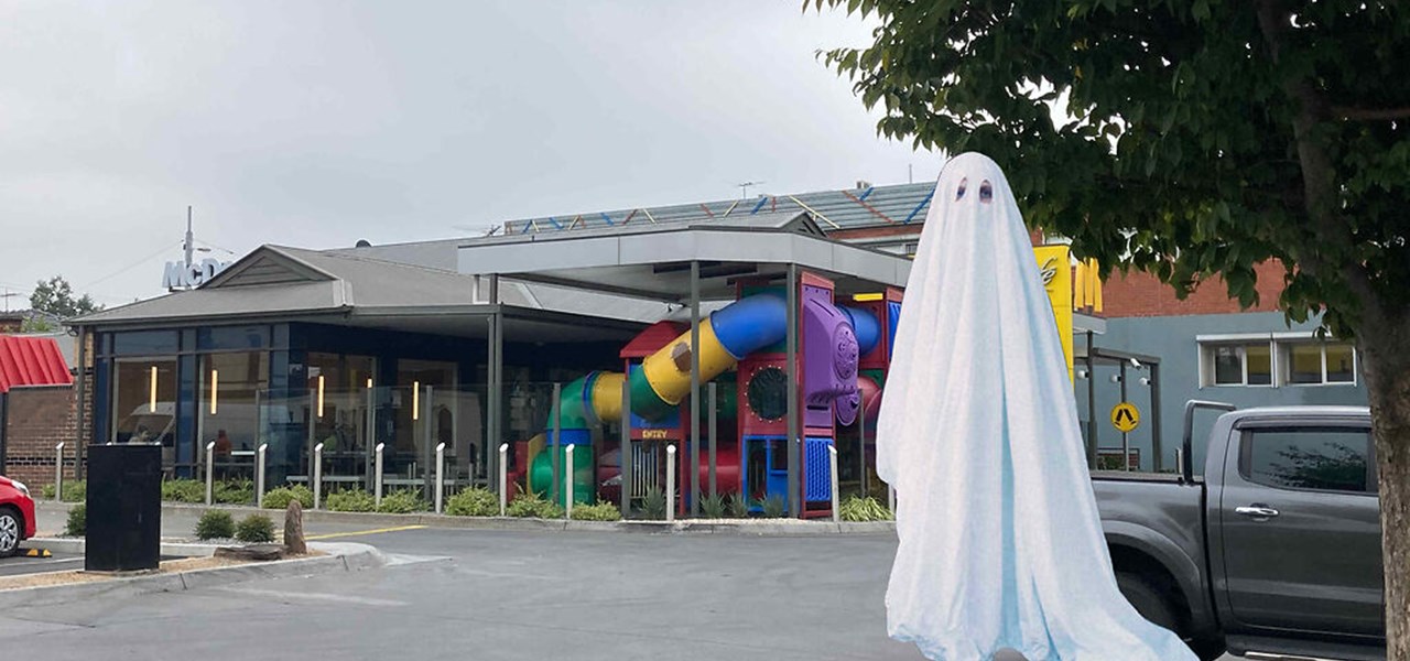 Ghost-like person in a sheet (with 2 eye holes) in the car park of a building (perhaps a retirement village)