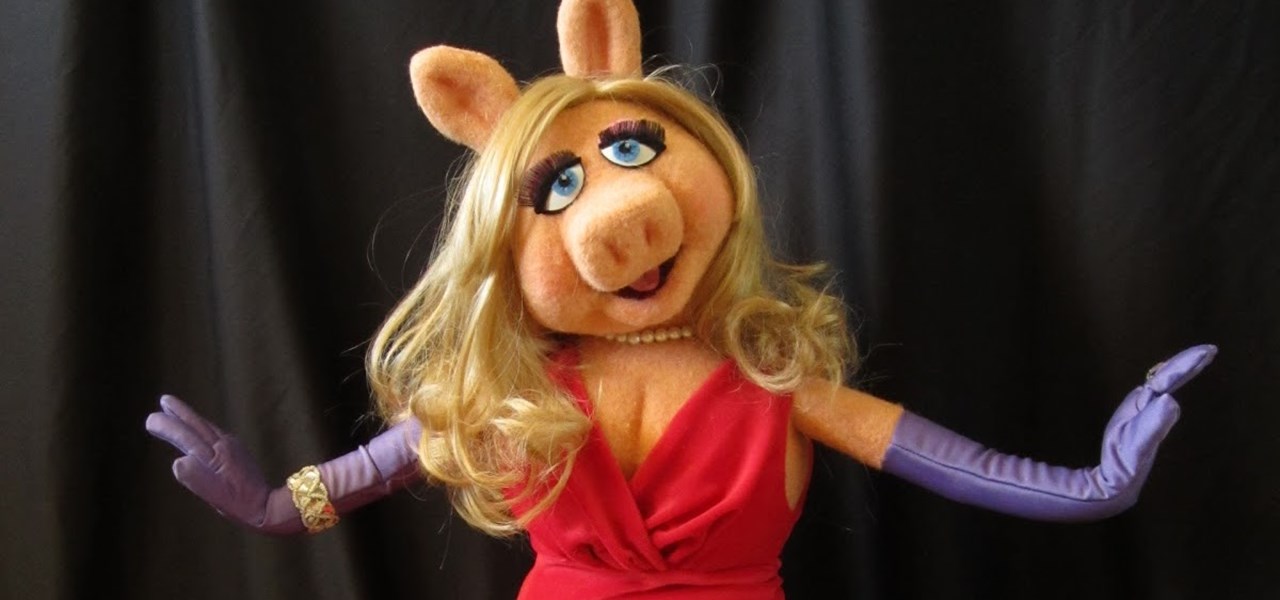 Performer wearing a Miss Piggy mask, red dress and mauve gloves in front of a black curtain